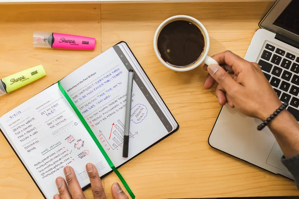 A notebook, highlighters and a coffee on a wooden desk