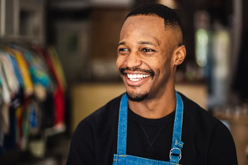A shop owner in a denim apron laughing in his clothing store