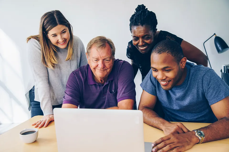 Four people gathered around a laptop, smiling