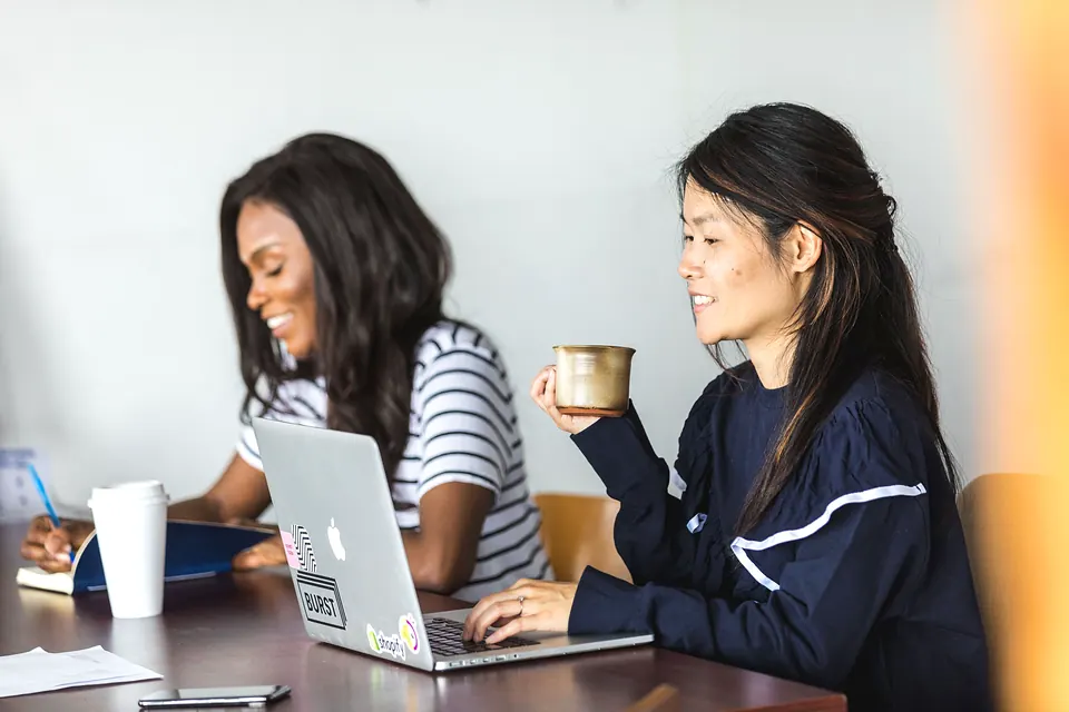 Two women laughing as they work together at a laptop
