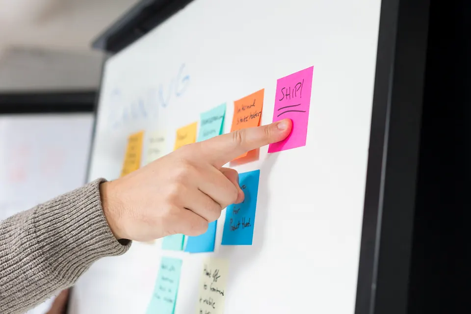A hand pointing at coloured sticky notes on a whiteboard