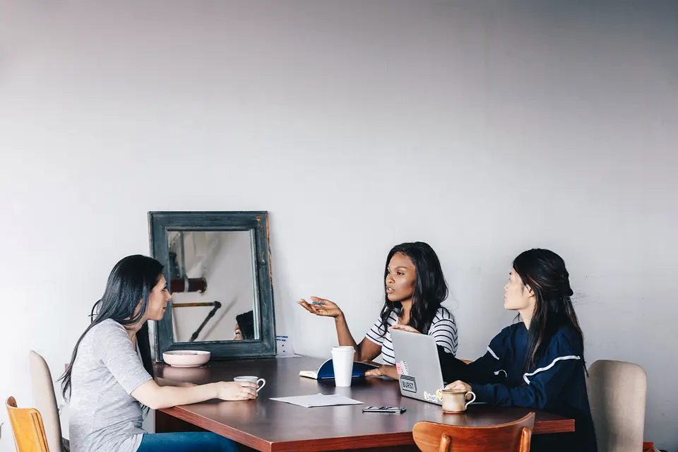 Three women talking around a wooden table