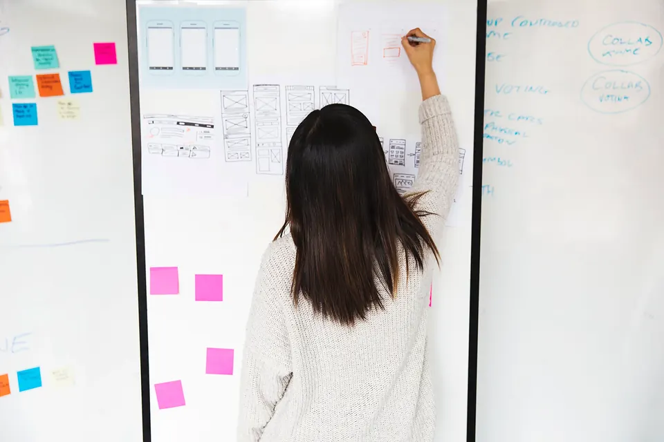 A designer sketching website layouts on a whiteboard covered in sticky notes